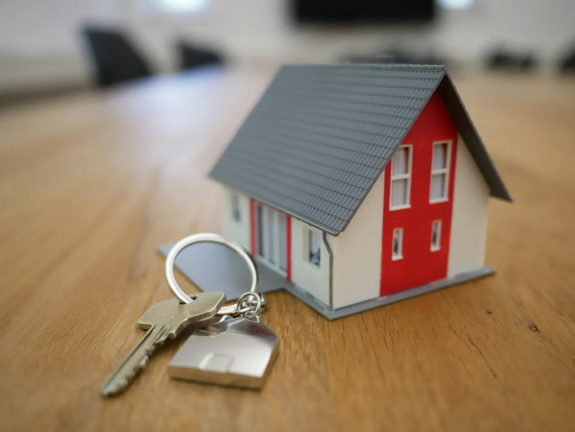 A set of house keys resting beside a model home on a timber table