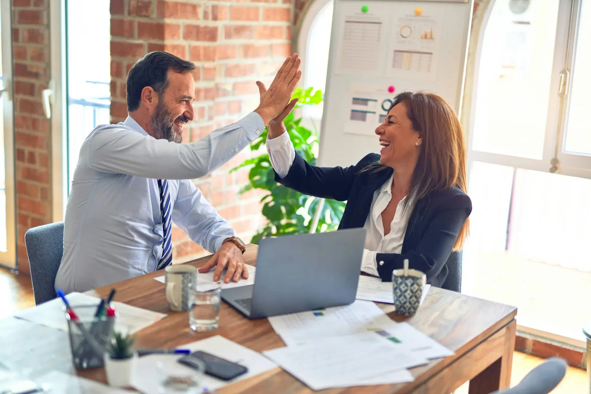 Two property managers high-fiving across a desk in a bright office